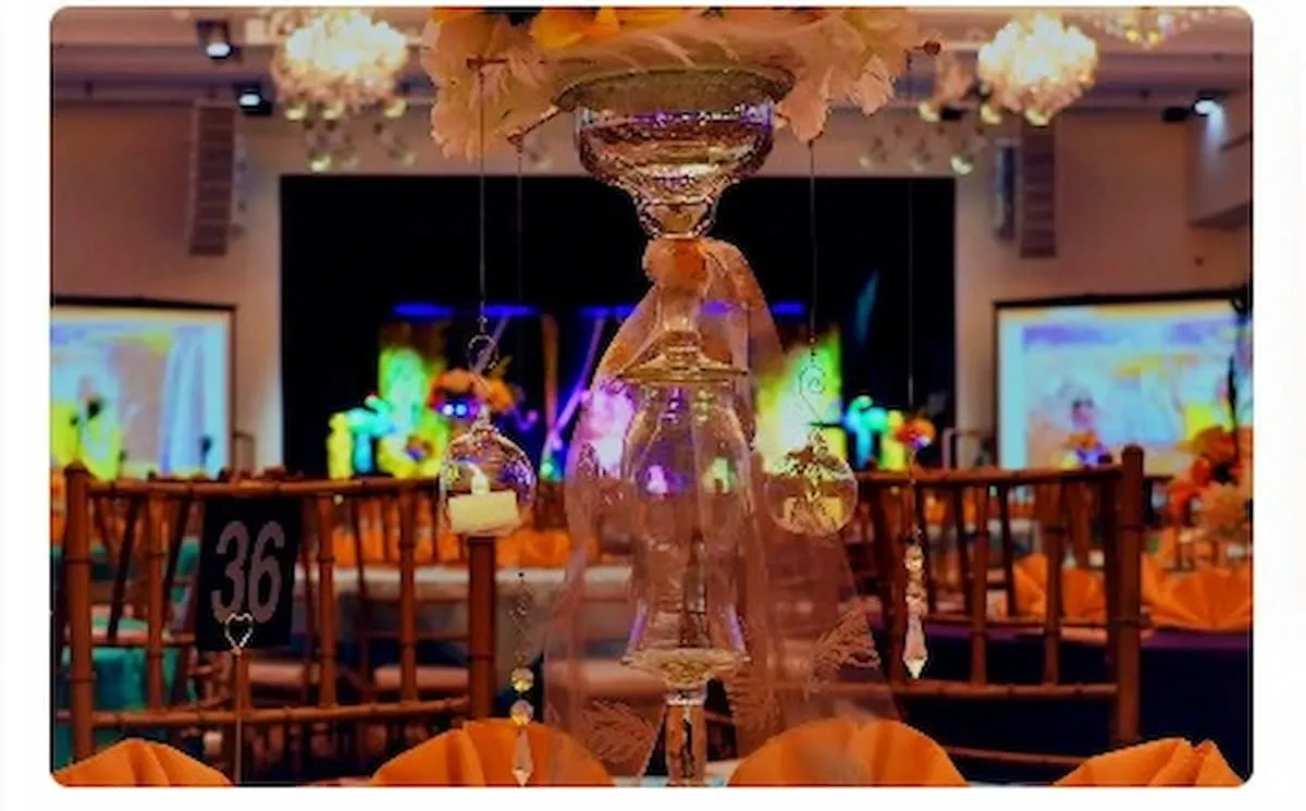 A spacious banquet hall set for a reception, featuring round tables with white cloths, yellow floral centerpieces, and abundant natural light, creating a warm and inviting atmosphere.