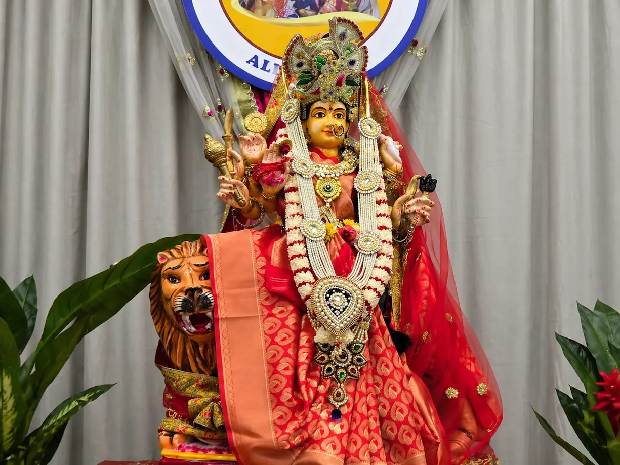 Devotee performing a ritual offering to a decorated Goddess Durga murti inside a temple setting.