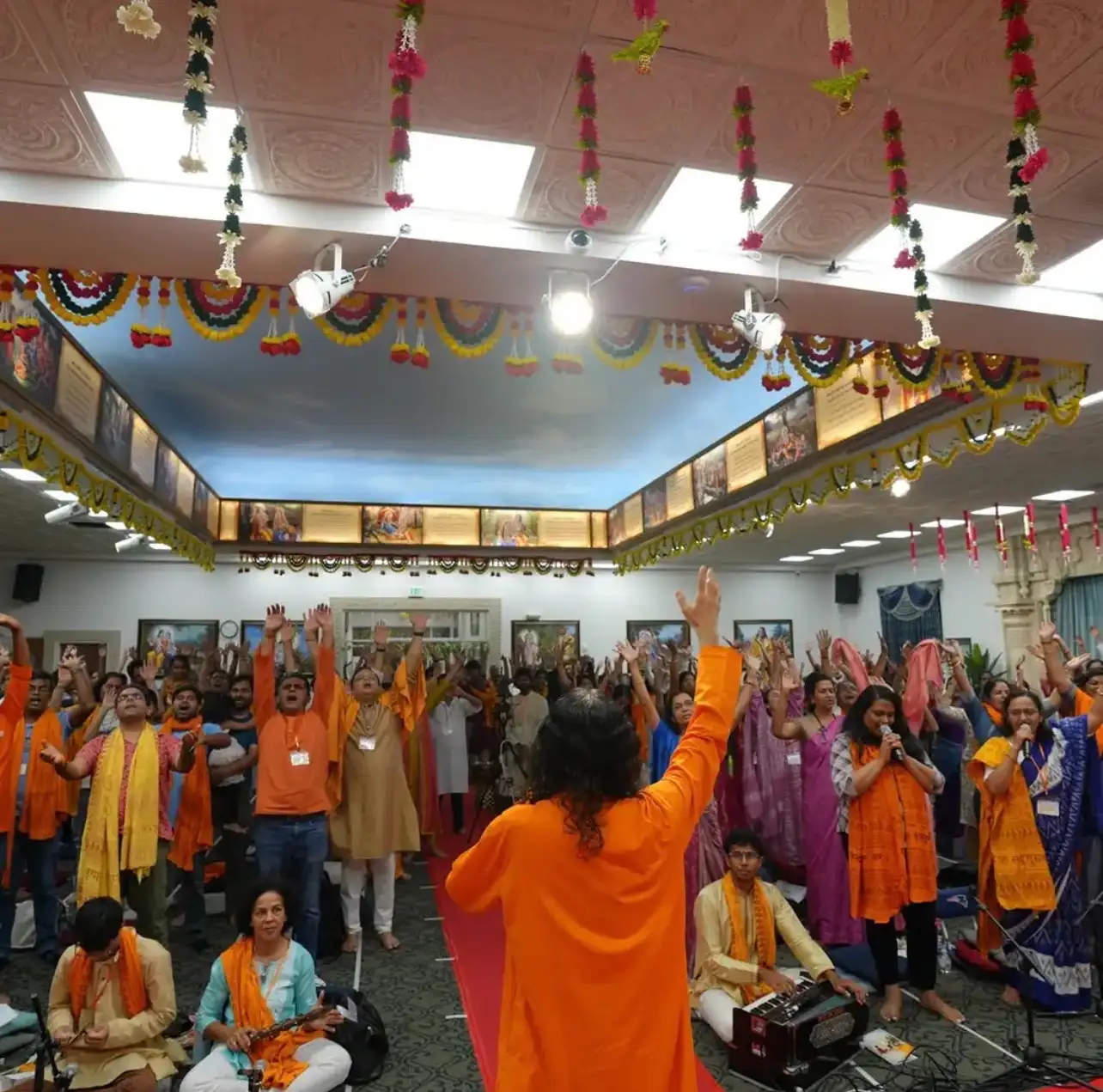 A large gathering of devotees standing with raised hands and folded palms during a devotional satsang at the Dallas Spiritual Retreat