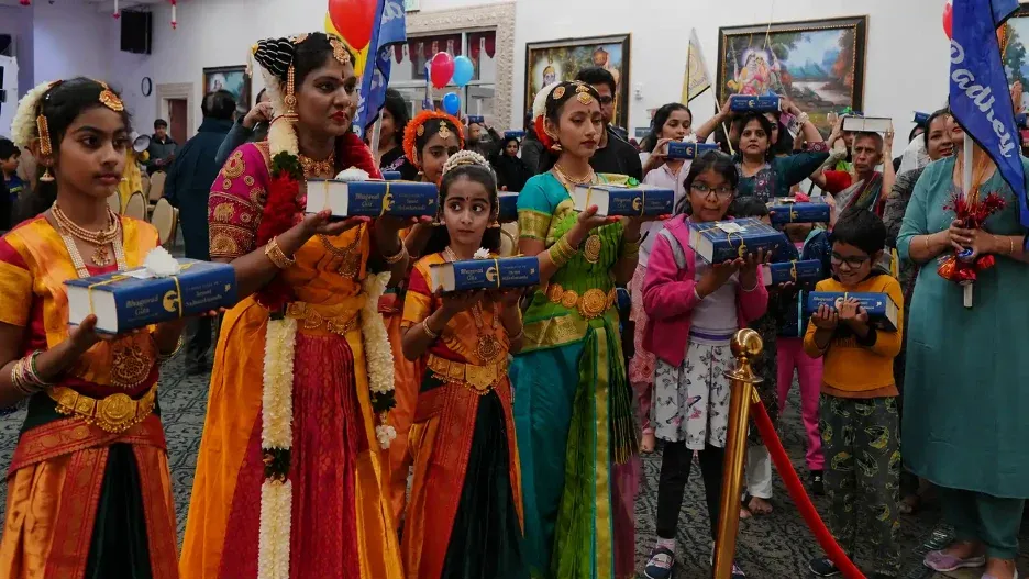 Devotees in traditional attire holding Bhagavad Gita books during a ceremonial procession at Radha Krishna Temple of Dallas