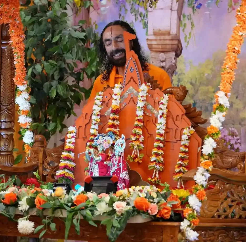 Swami Mukundananda joyfully leading the midnight Janmashtami celebration before beautifully decorated baby Krishna deities, surrounded by flowers and devotional decorations